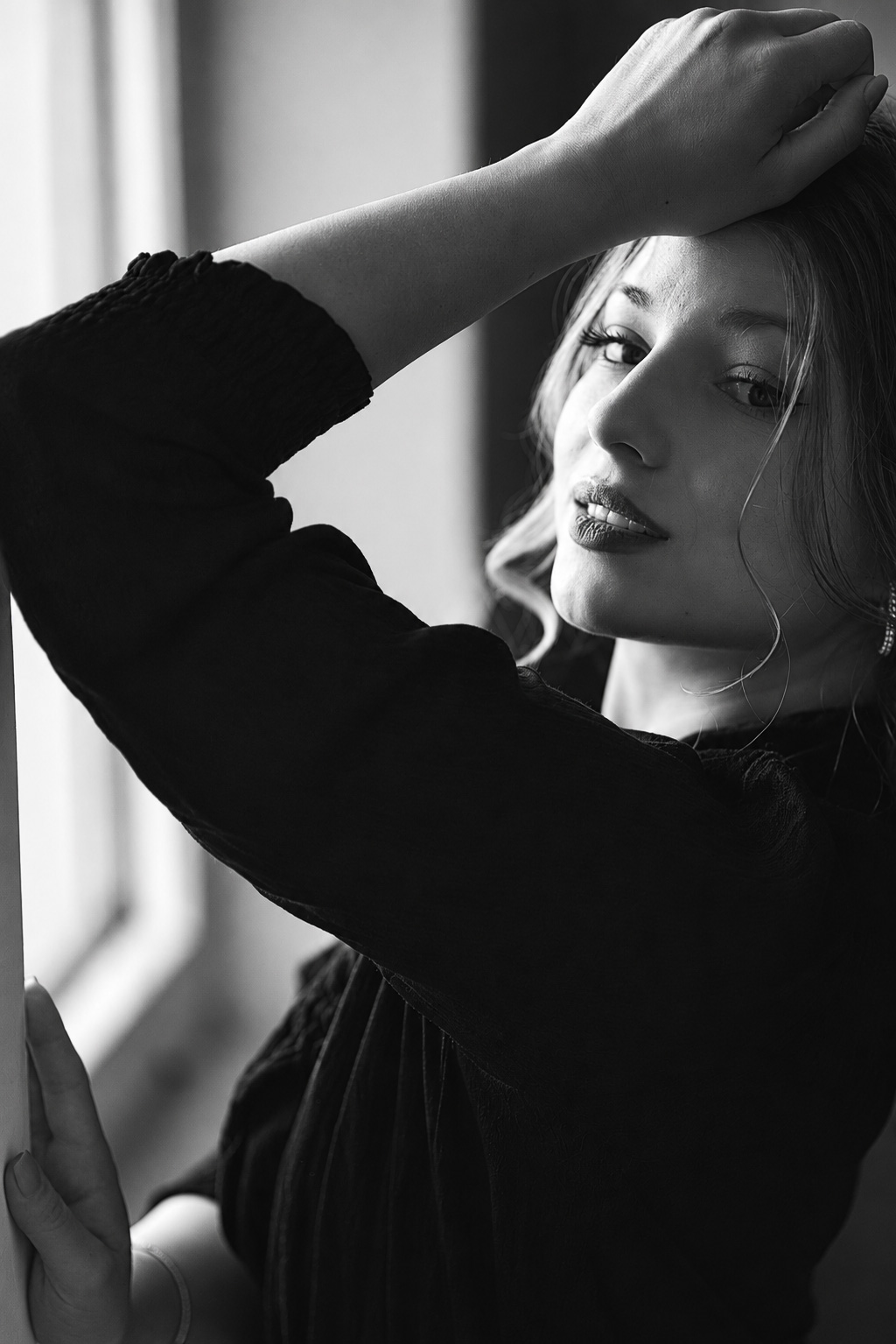 Black-and-white window-light portrait of a woman with one arm raised above her head