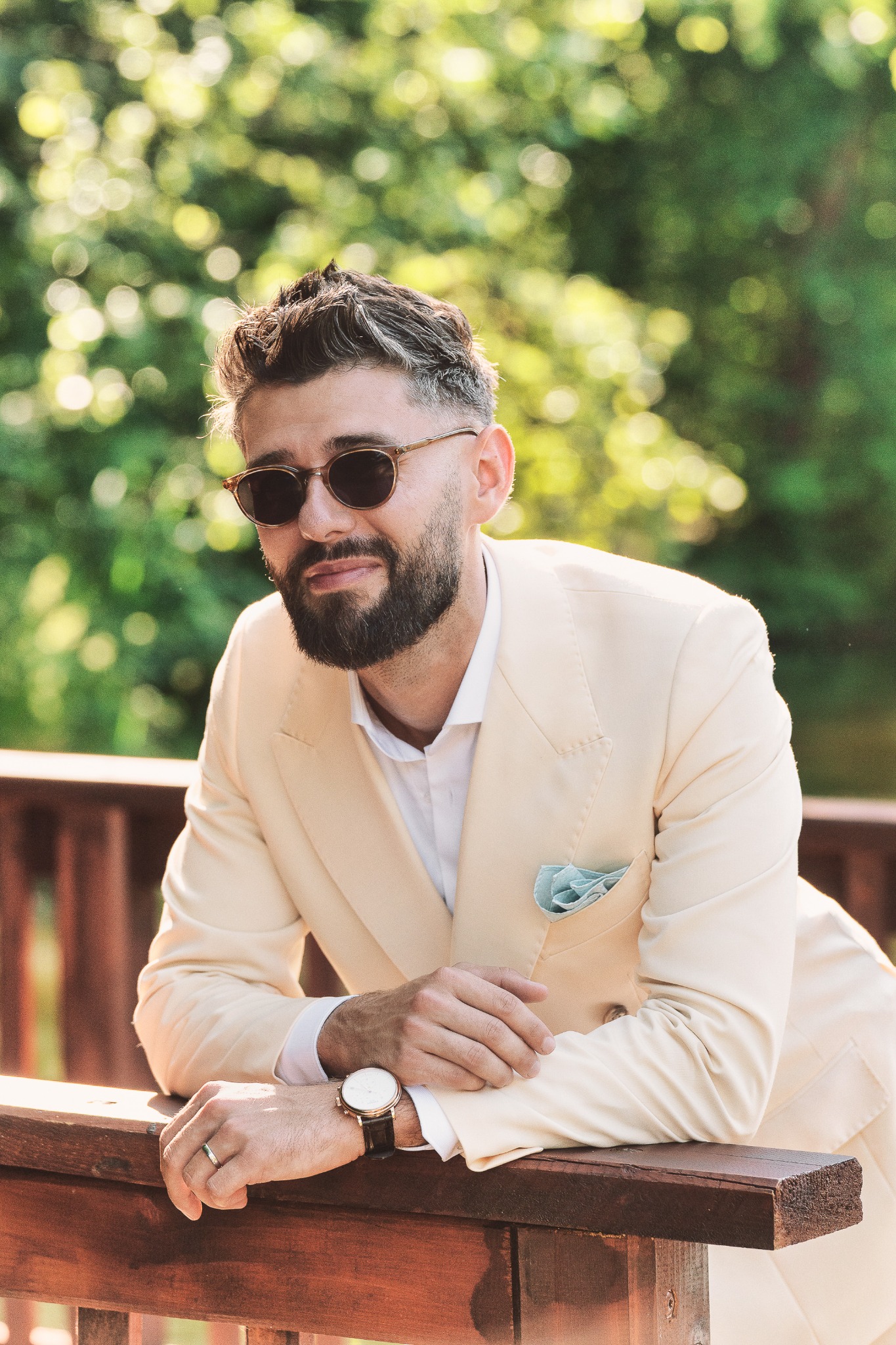 Groom in a cream suit and sunglasses beside a wooden railing